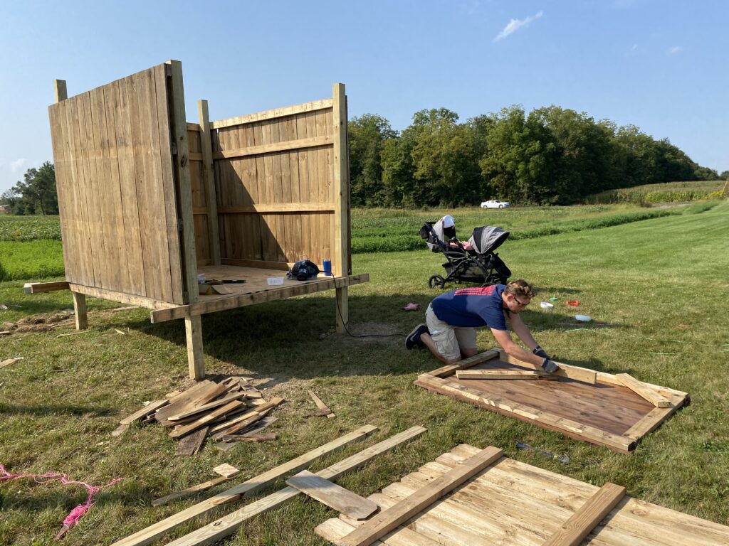 Man building a chicken coop door outside on a sunny day as part of the City Folk Homestead story 