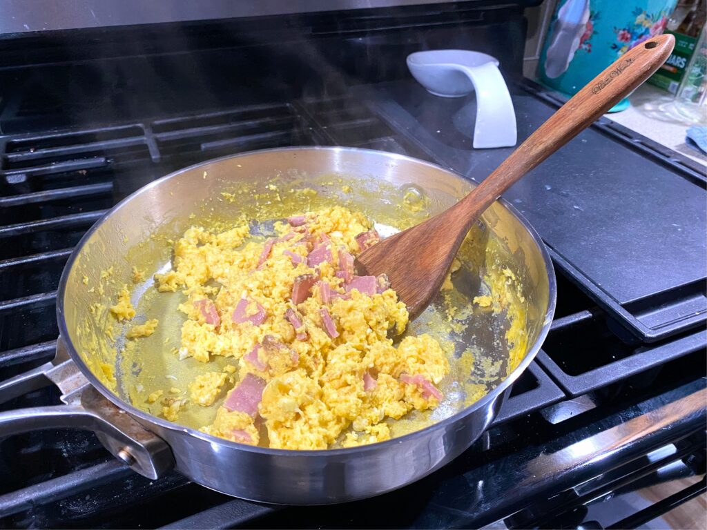 Cooked Egg, ham, and cheese scrambled eggs in a skillet with a wooden serving spoon