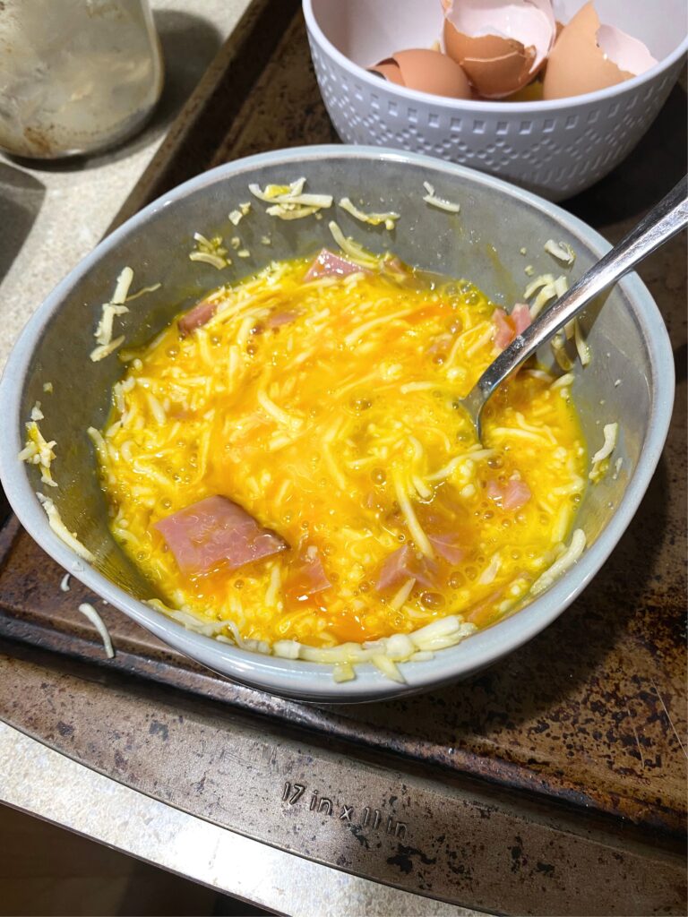 Scrambled eggs uncooked mixed with ham and cheese in a bowl