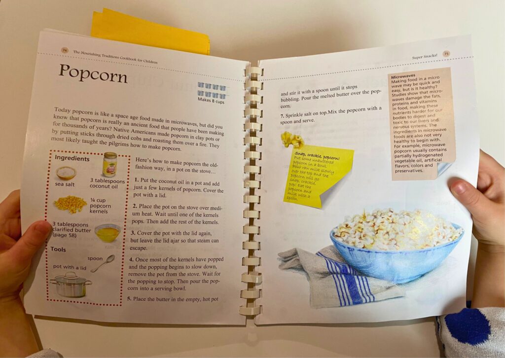 Child holding Nourishing Traditions Cookbook for Children open to page on homemade popcorn