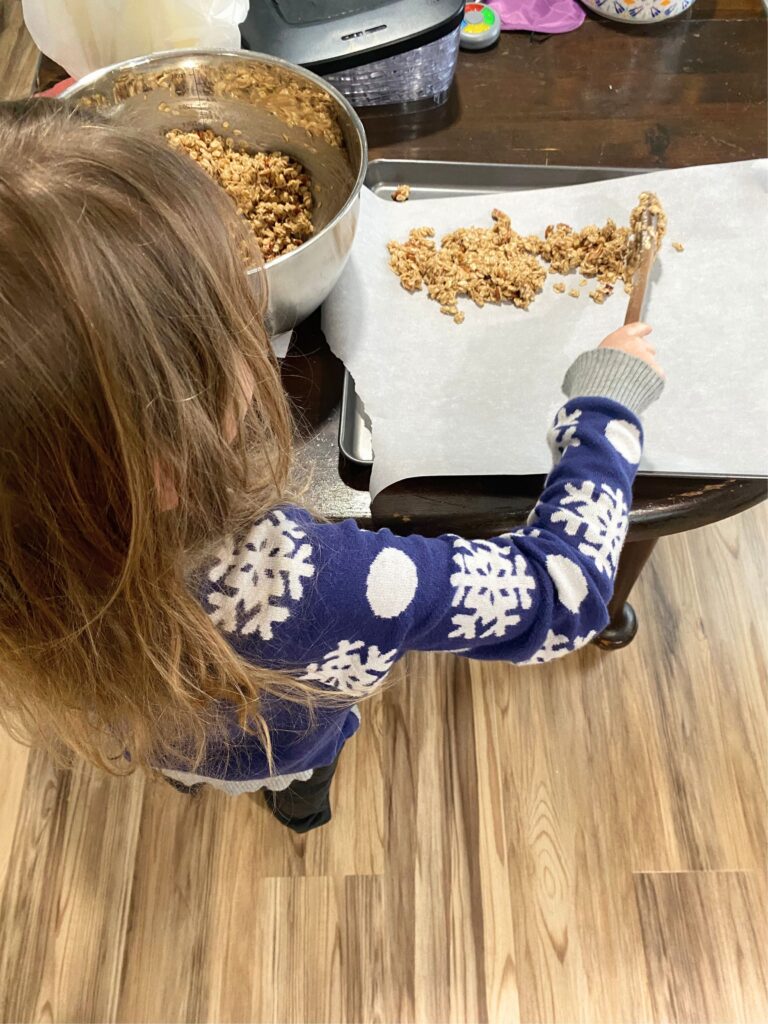 little girl spooning homemade granola onto a baking sheet in the kitchen