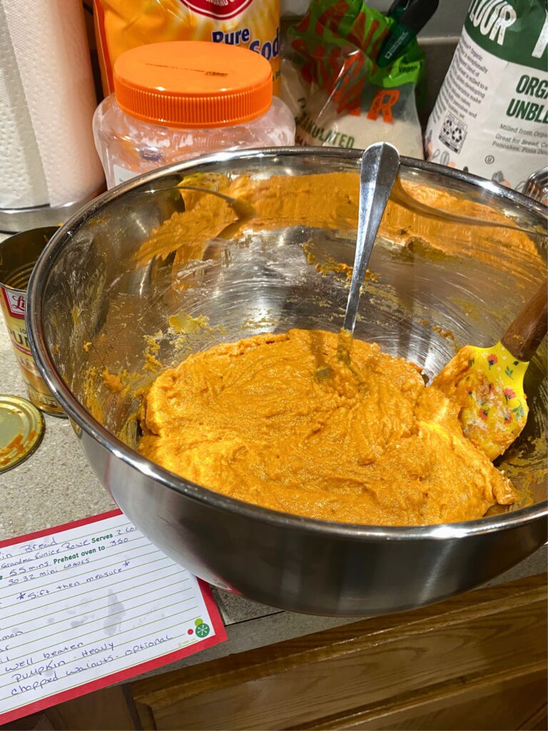 Pumpkin bread batter in a stainless steel bowl with a spoon and a spatula