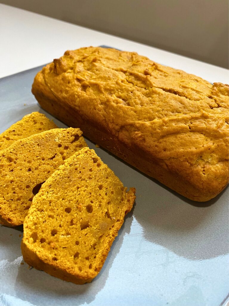 From the right angle, a close up of a full pumpkin bread loaf uncut and three cut pumpkin bread slices