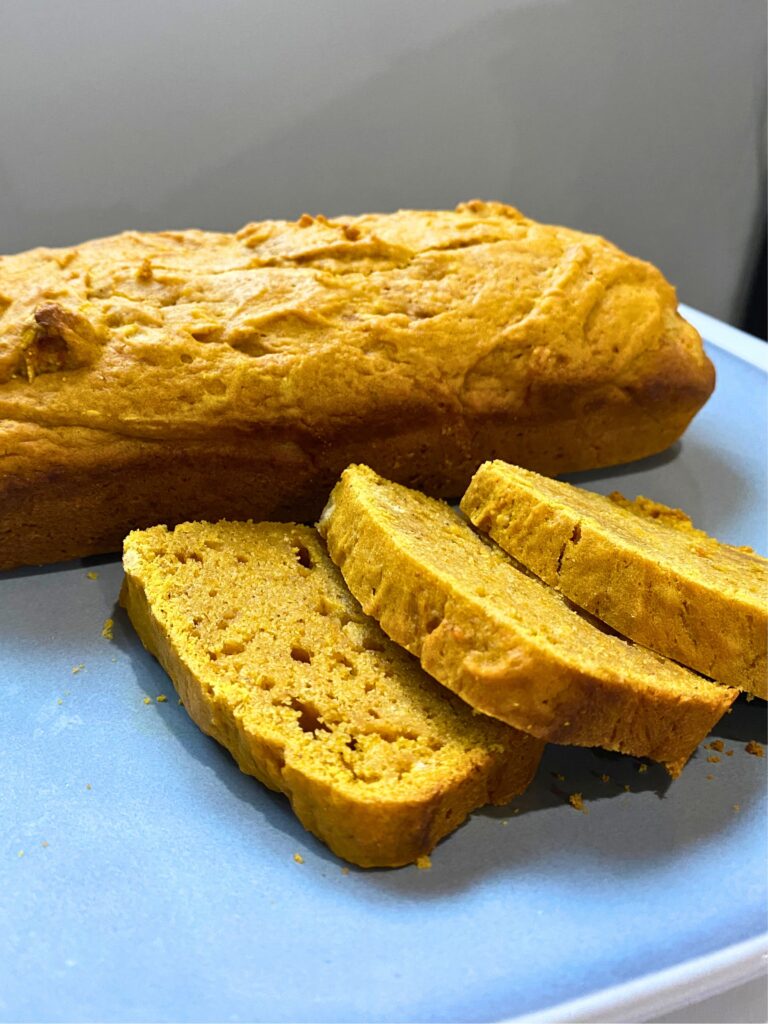 Close up of three slices of pumpkin bread in front of a full bread loaf on a grey plate