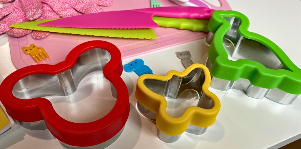 Mickey Mouse, butterfly, and dinosaur shaped sandwich cutters and yellow cat, blue elephant, and grey bear food picks on a table