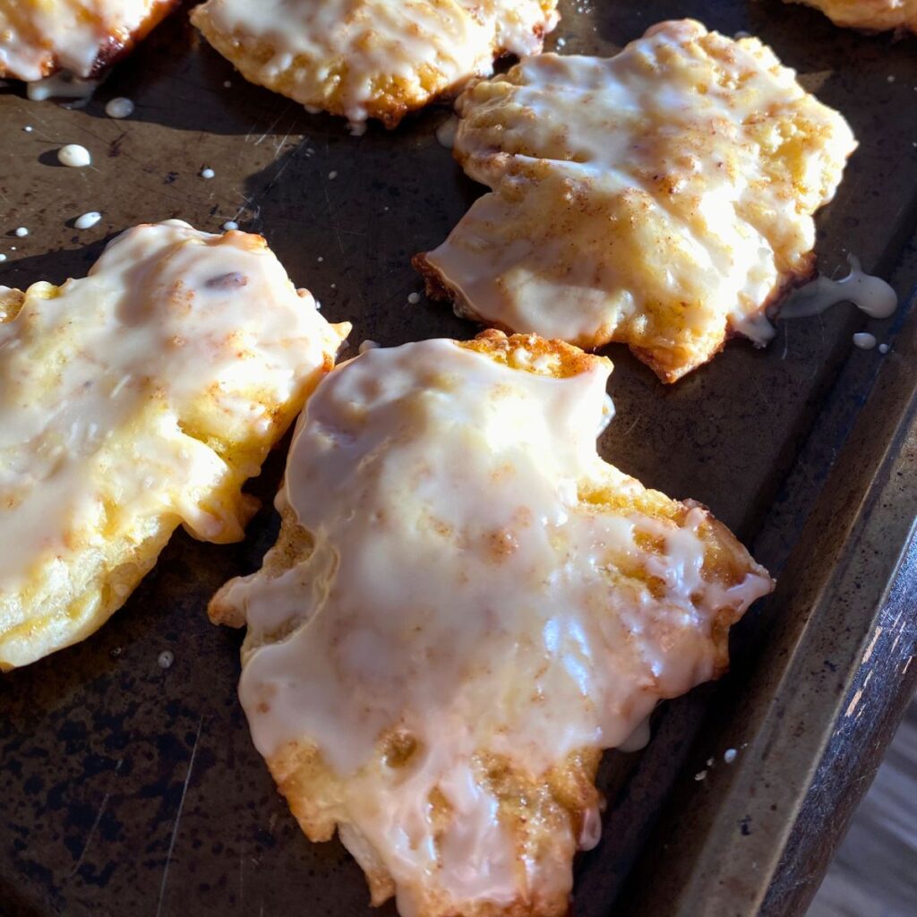 glazed apple pie filled hand pies in the shape of a leaf sitting on a baking sheet 