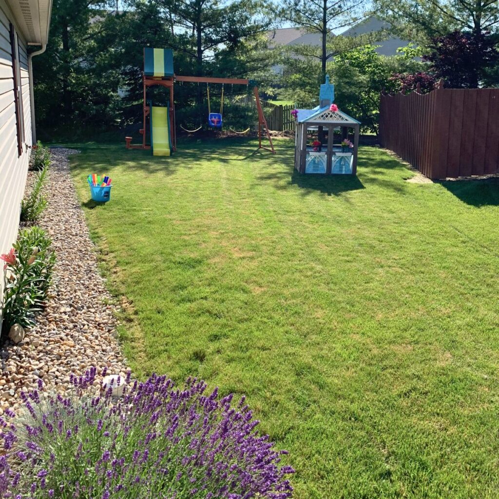 Playset and playhouse on the side of a suburban home with rock landscaping and freshly mowed grass