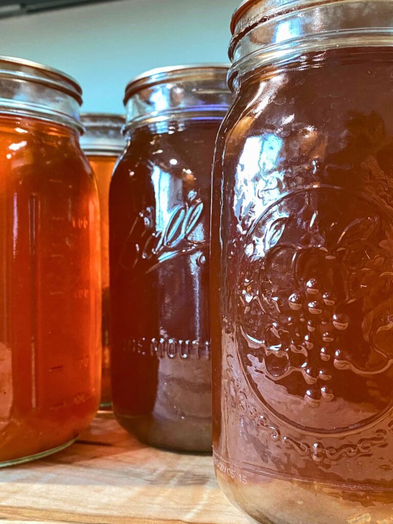 Four quarts of pressure canned vegetable broth stored on a wood tray in Ball wide-mouthed glass mason jars