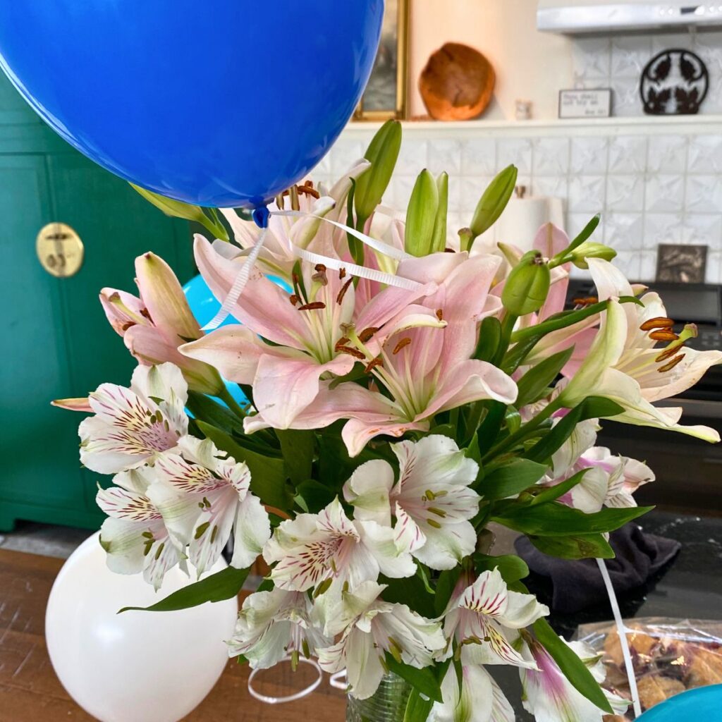 Pink lillies in a vase on a kitchen countertop tied with a blue balloon for a boy baby shower