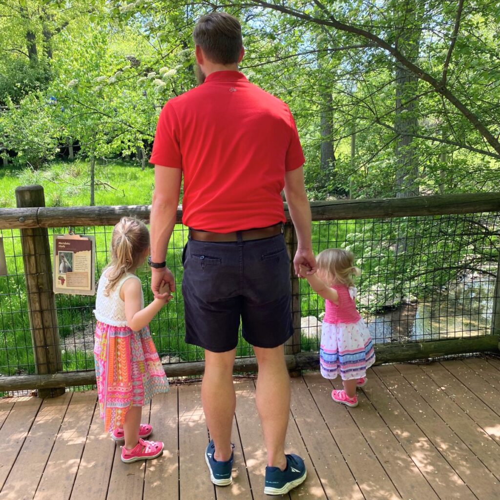 Man holding the hands of two little girls in dresses at the zoo