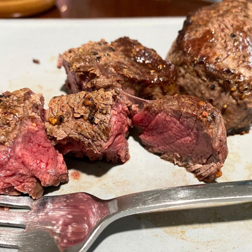 Up close medium rare steak cut in chunks and flaked with salt and pepper on a grey plate with a fork