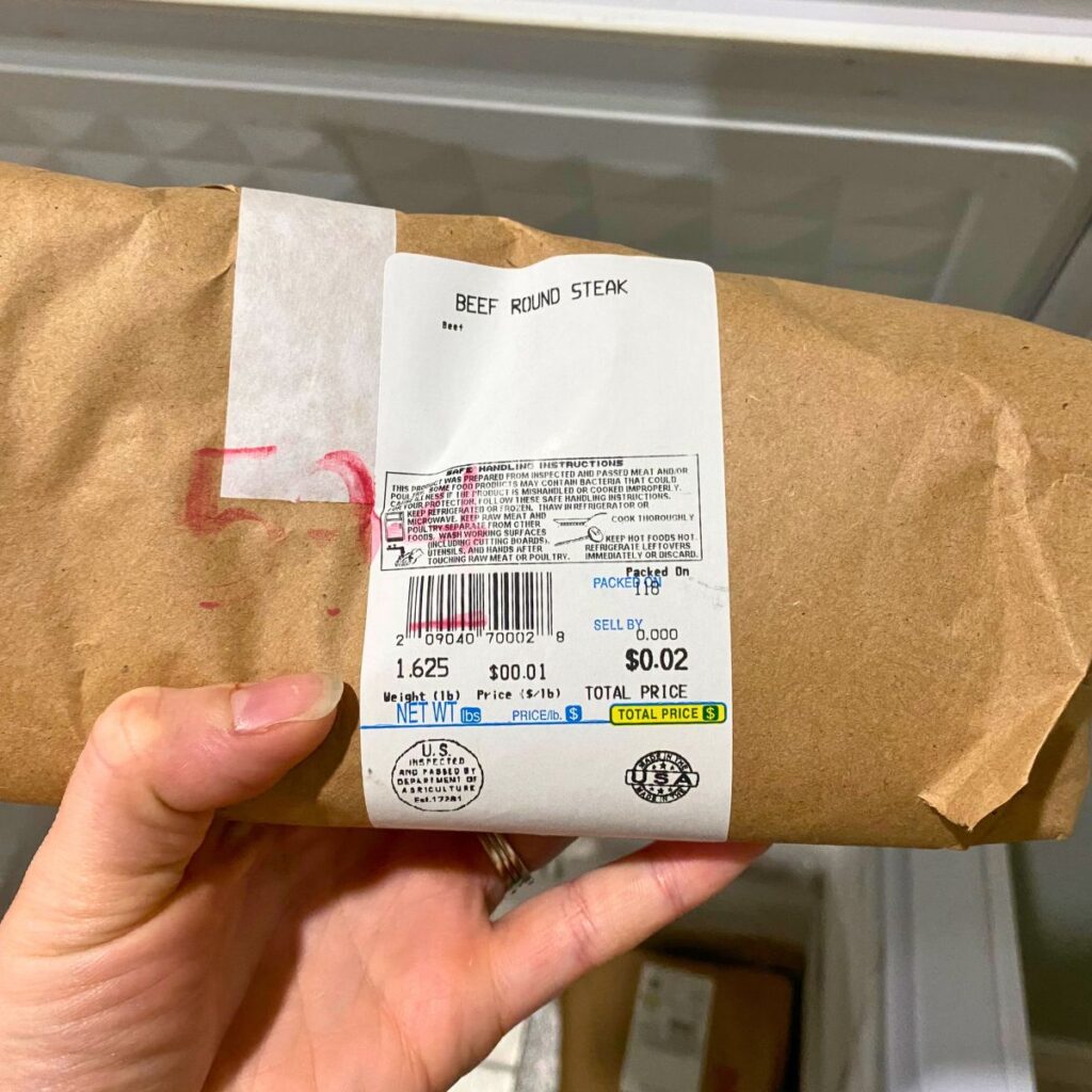 Hand holding beef round steak processed and prepared by a local butcher with the weight and label shown