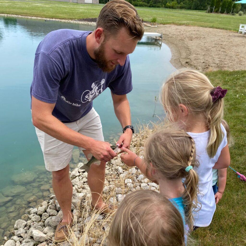 Man holding small-mouthed bass for three little girls to touch