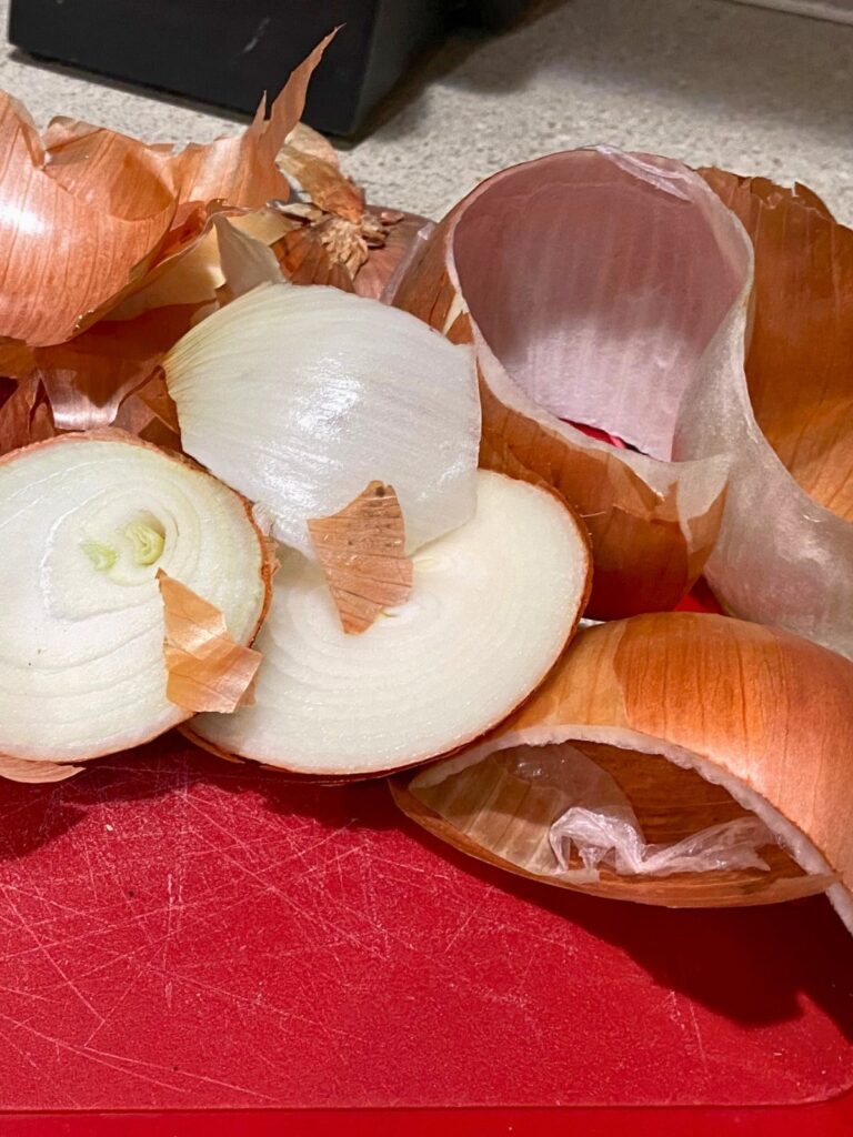 Yellow onion peels and scraps piled onto a red cutting board after preparing the raw onions for preservation through freezing