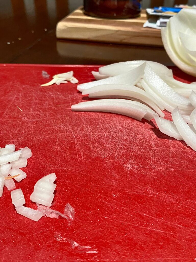 Raw yellow onions sliced and diced in small pieces on a red cutting board in two separate piles