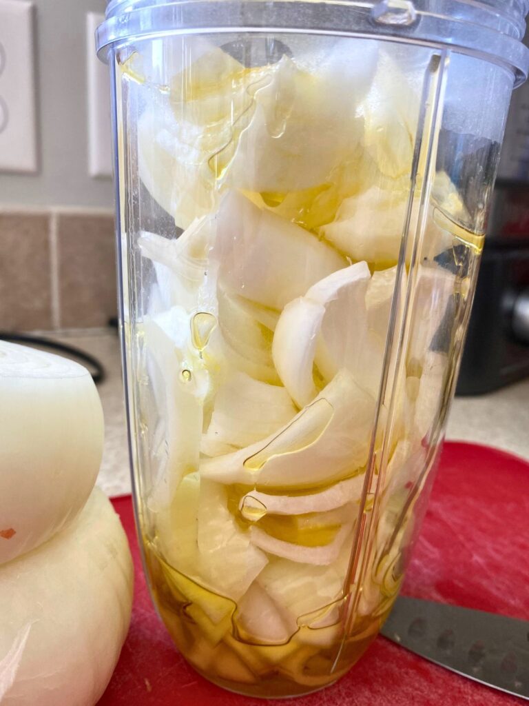 Roughly chopped onion slices in a blender cup with olive oil