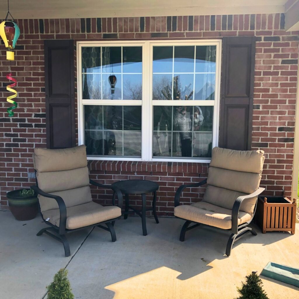 The front porch of a brick home with two chairs and a small circular table in the middle