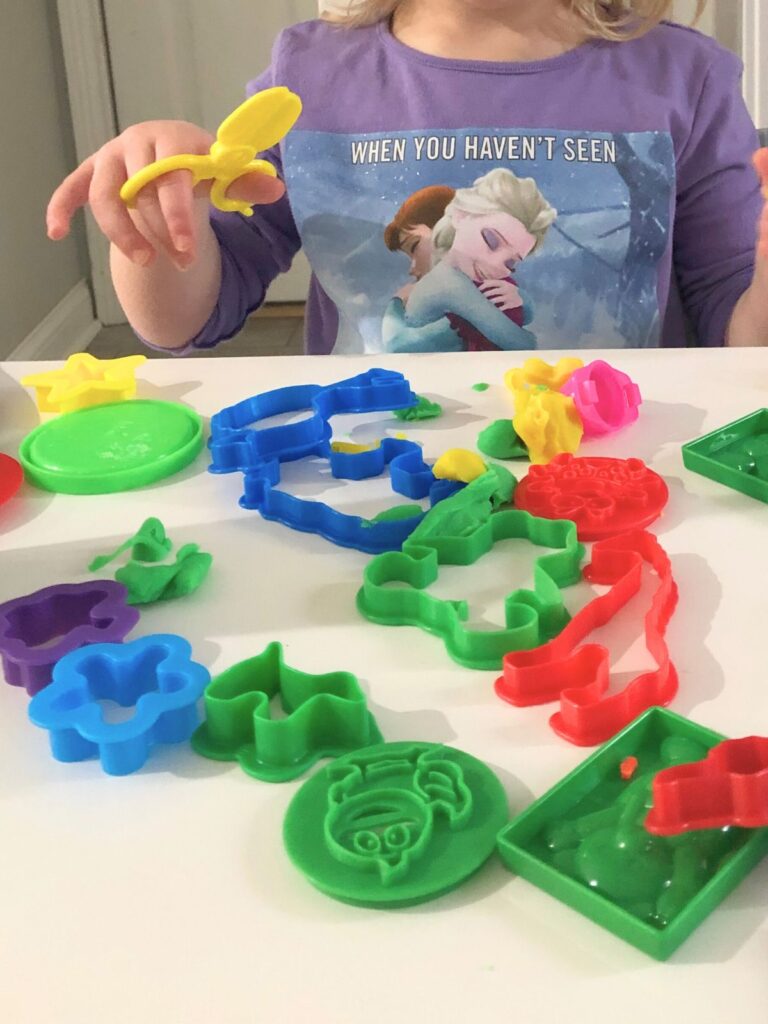 Young toddler playing at the kitchen table with play doh and accessories like scissors and animal cut outs