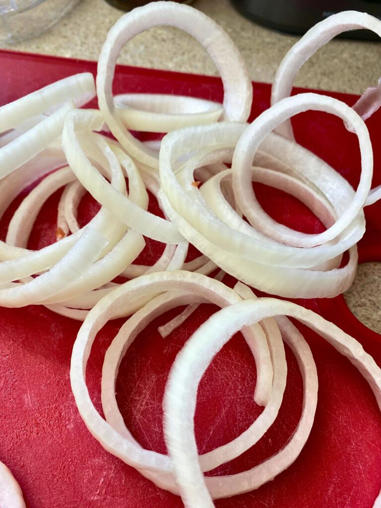 Raw yellow onions cut into rings piled onto a red cutting board