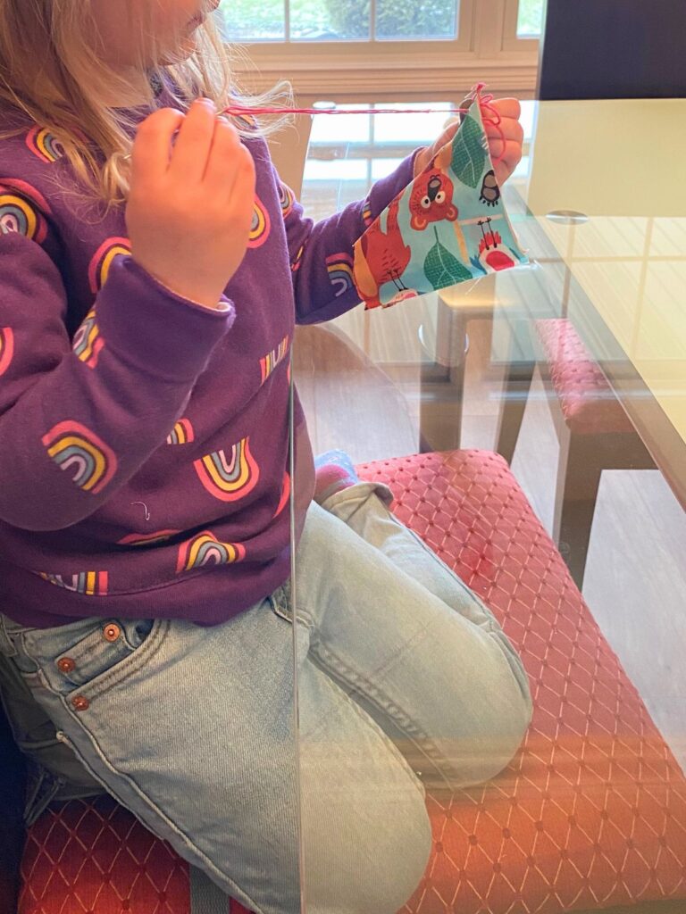 Young child learning to sew a doll's pillowcase with thick thread and a plastic needle on a winter day