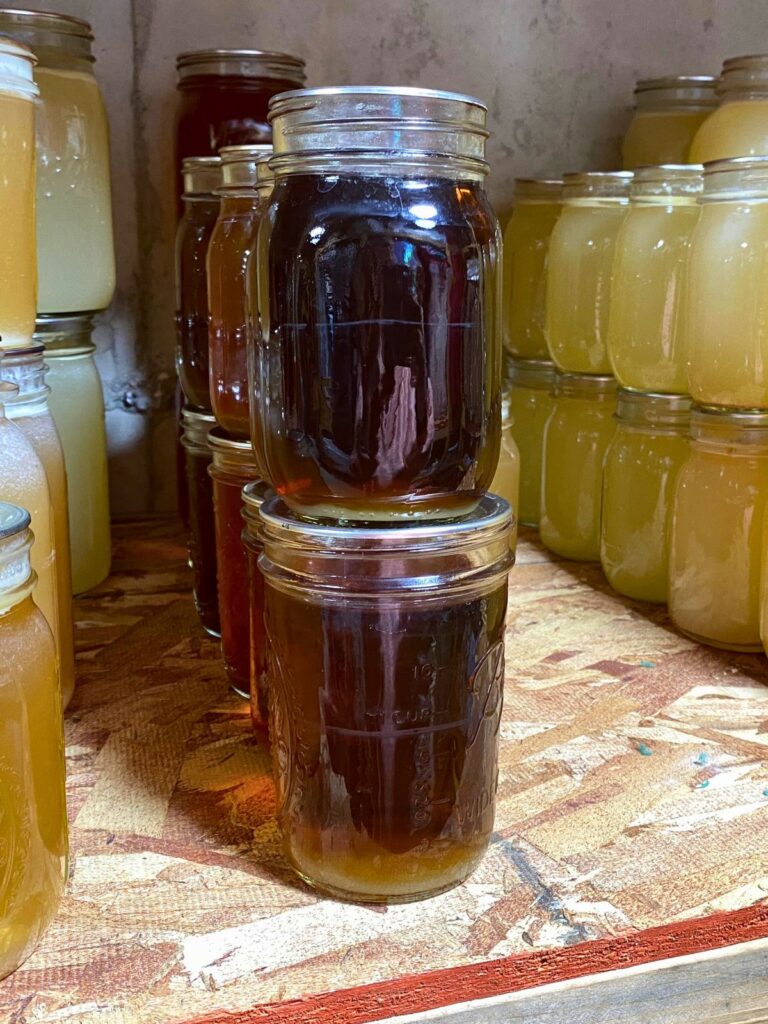 Rows of pressure canned broths stacked two high on a pantry shelf. 