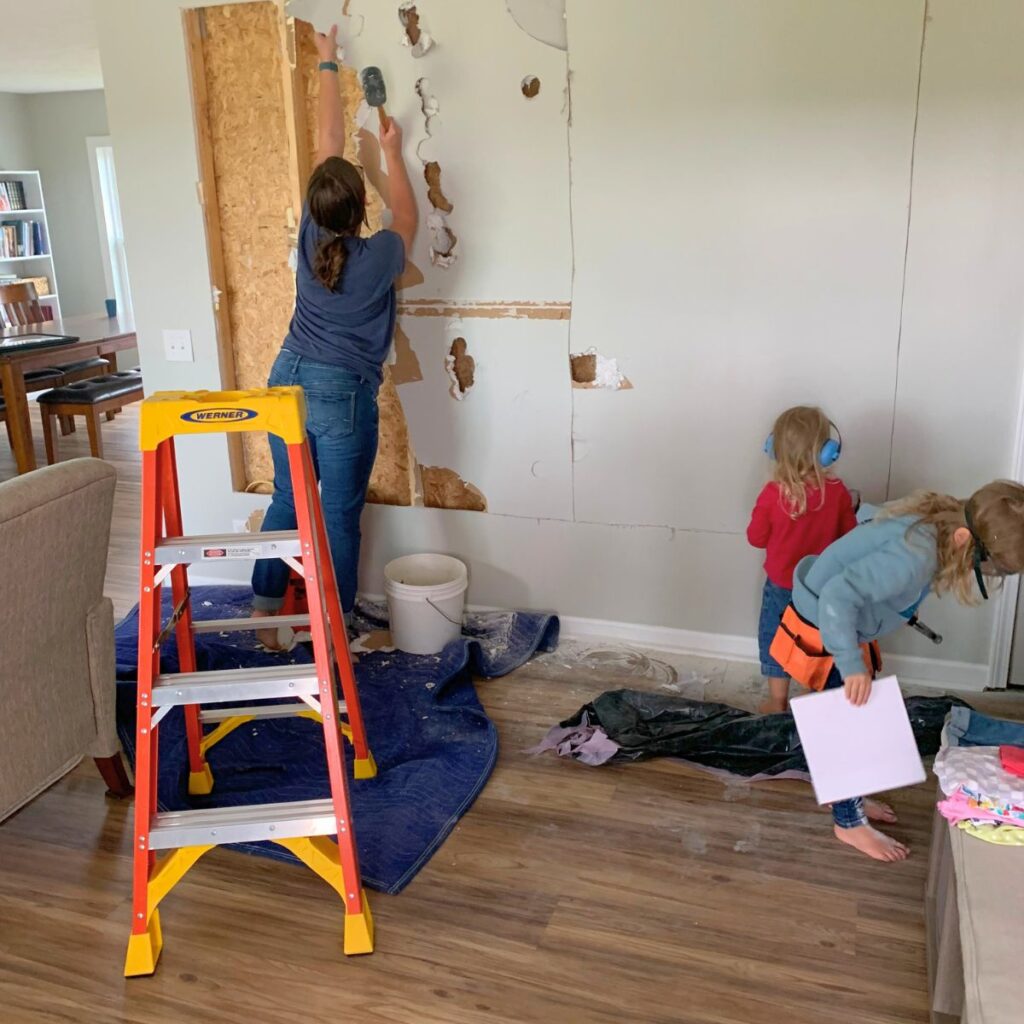 Woman knocking holes in drywall with two small children helping her