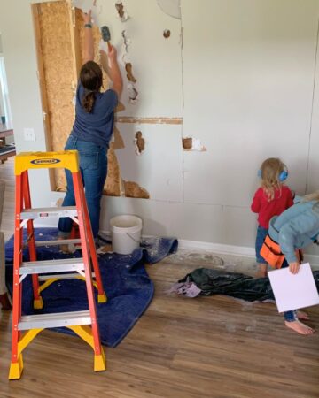 woman taking down drywall with two children working beside her in safety goggles