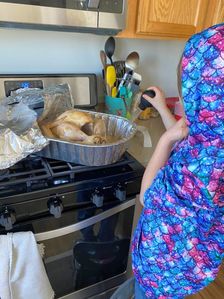 Young child standing on a stool at the stove in the kitchen basting a turkey