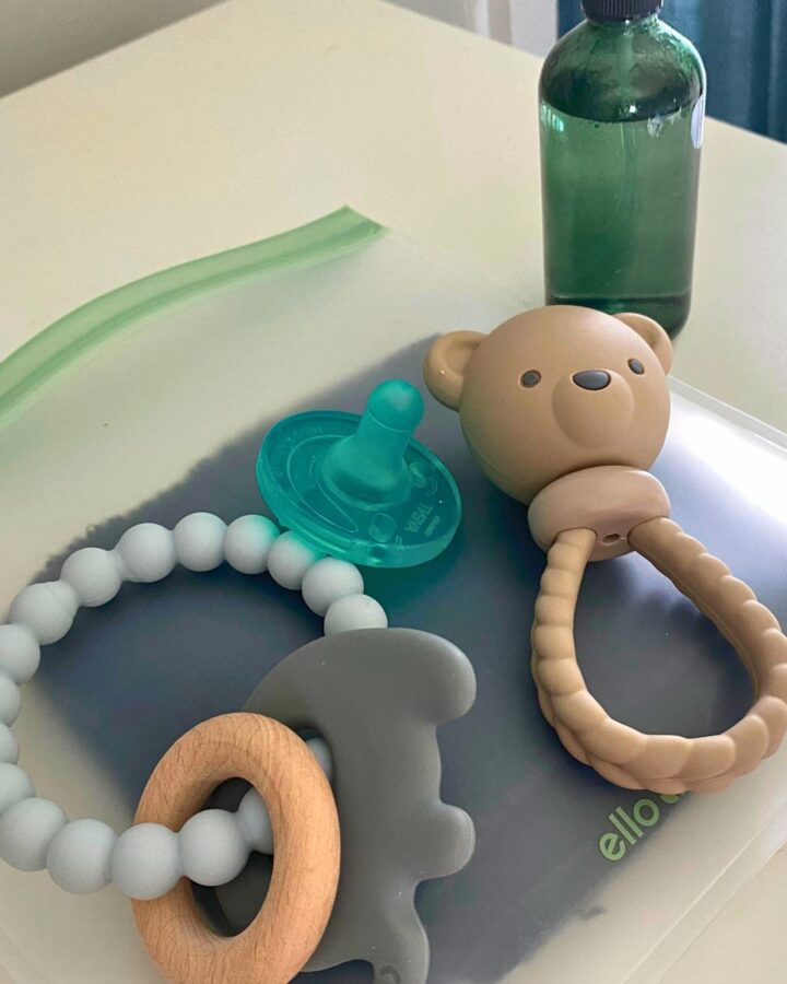 Clean silicone baby toys and pacifier on a white dresser with a glass spray bottle filled with vinegar cleaning solution in the background