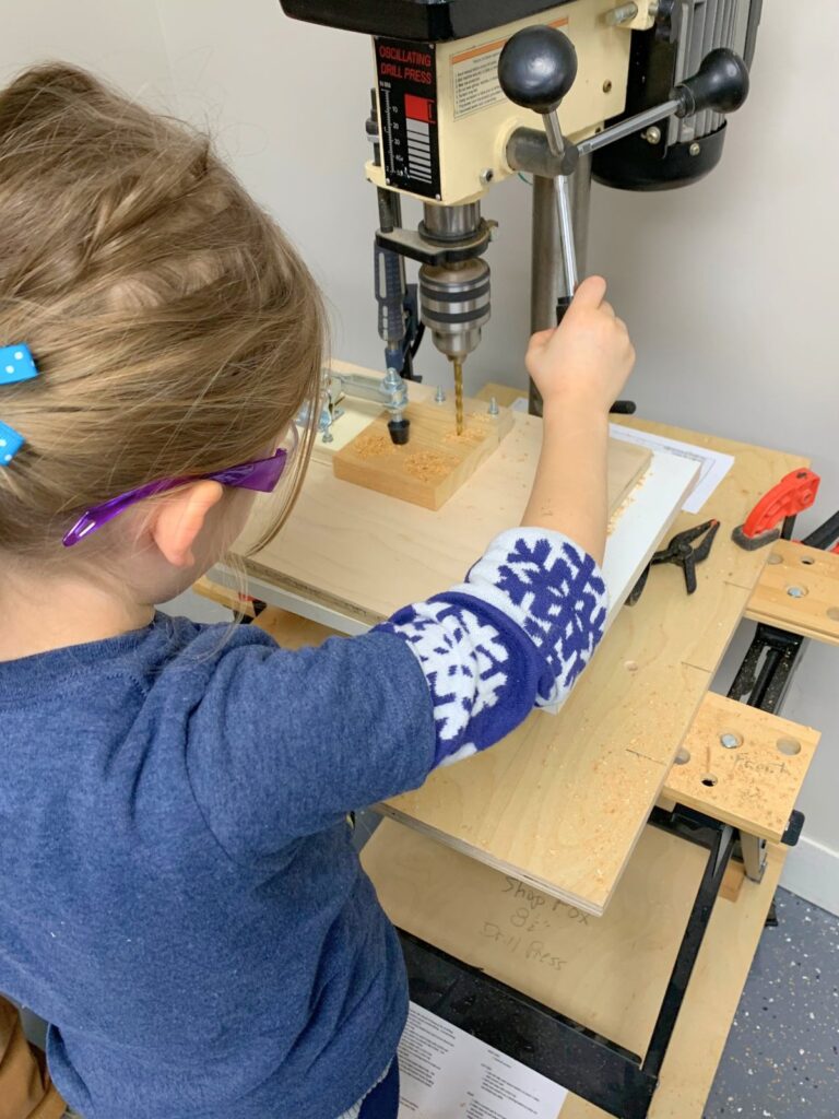 Young girl using a drill press in a woodworking workshop